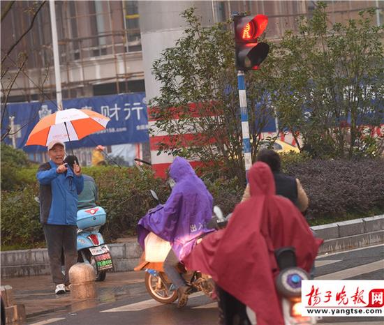 退休老人雨中撑伞劝行人不要闯红灯